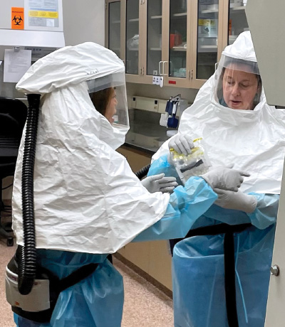 Photo of people working in a lab in hazmat gear. 